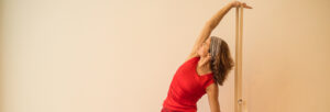 Yogalehrerin Annette in roter Kleidung in Yogahaltung mit Gurt